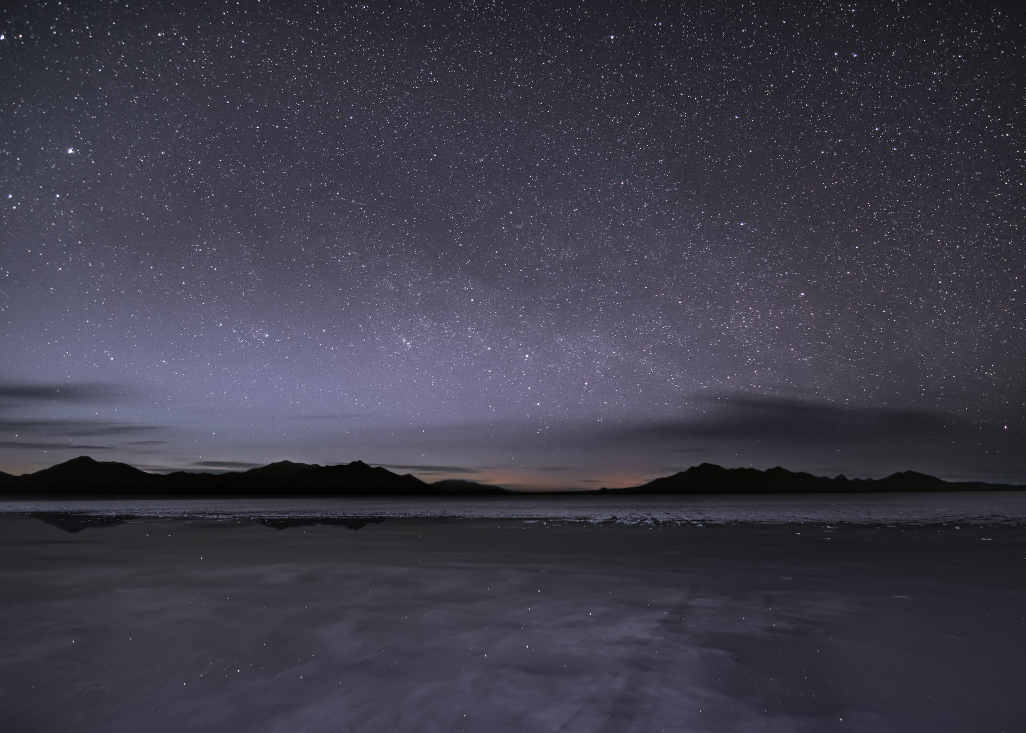 The stars are reflected in water sitting on the salt flats from recent rain